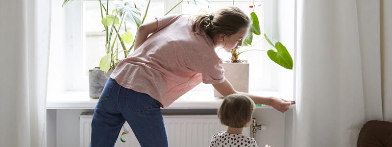 En mamma med sitt barn justerar v&auml;rmen p&aring; ett element.