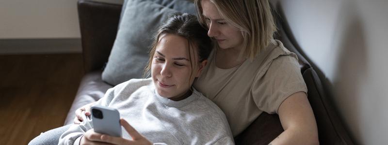Tv&aring; unga kvinnor sitter i soffa och tittar p&aring; mobil