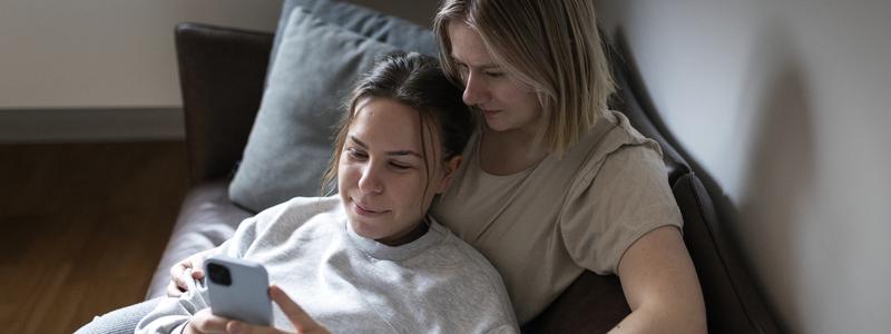 Tv&aring; unga kvinnor sitter i soffa och tittar p&aring; mobil